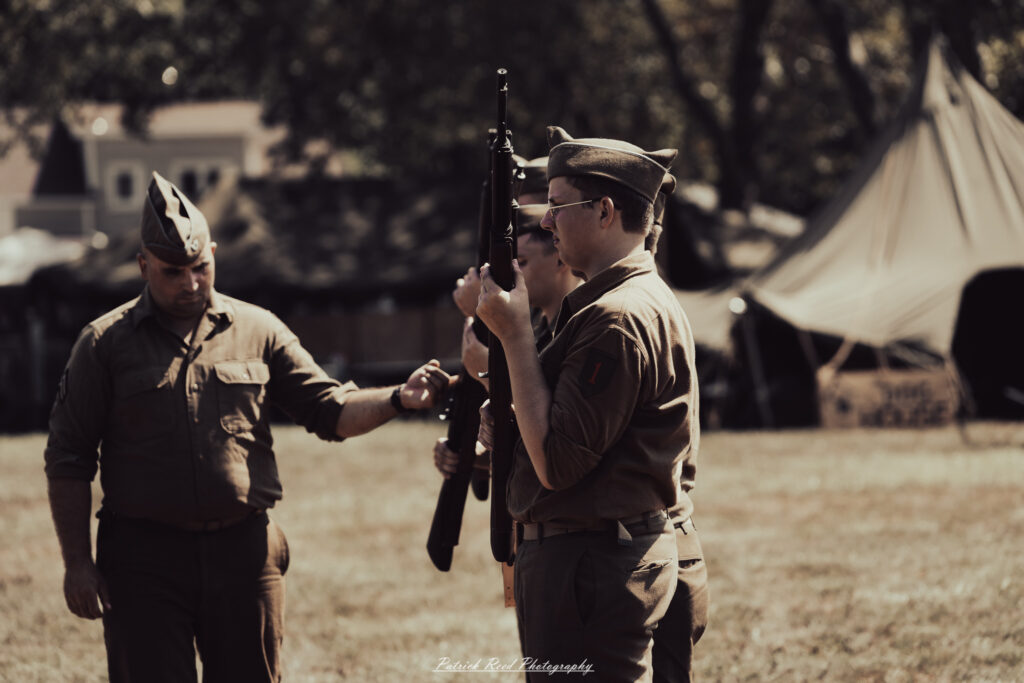 A group of World War II reenactors in period-accurate uniforms—American, German, and French Resistance—on a sandy shore during the D-Day Conneaut 2025 reenactment at Conneaut Township Park, Ohio.