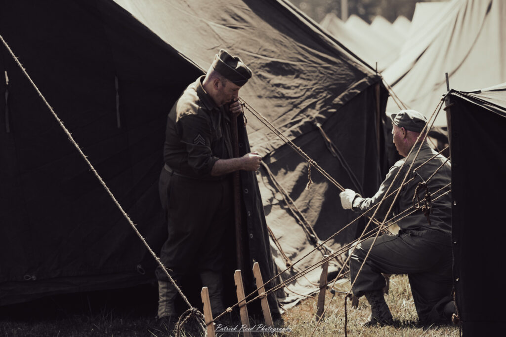 A group of World War II reenactors in period-accurate uniforms—American, German, and French Resistance—on a sandy shore during the D-Day Conneaut 2025 reenactment at Conneaut Township Park, Ohio.