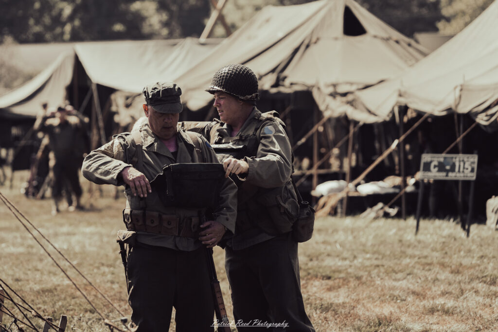 A group of World War II reenactors in period-accurate uniforms—American, German, and French Resistance—on a sandy shore during the D-Day Conneaut 2025 reenactment at Conneaut Township Park, Ohio.
