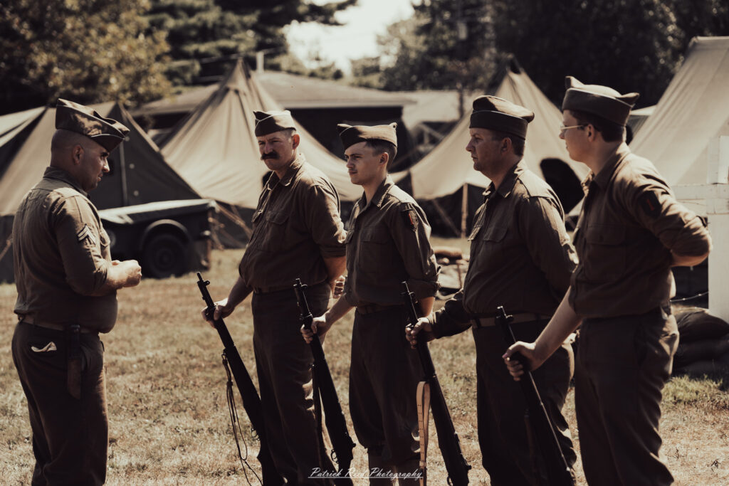 A group of World War II reenactors in period-accurate uniforms—American, German, and French Resistance—on a sandy shore during the D-Day Conneaut 2025 reenactment at Conneaut Township Park, Ohio.