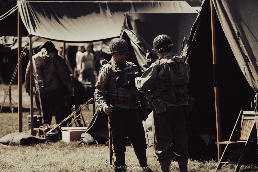 A group of World War II reenactors in period-accurate uniforms—American, German, and French Resistance—on a sandy shore during the D-Day Conneaut 2025 reenactment at Conneaut Township Park, Ohio.