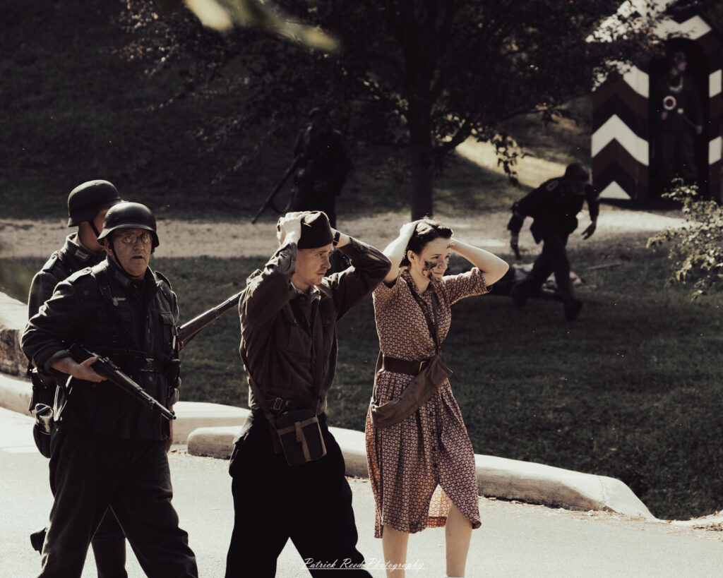 A group of World War II reenactors in period-accurate uniforms—American, German, and French Resistance—on a sandy shore during the D-Day Conneaut 2025 reenactment at Conneaut Township Park, Ohio.