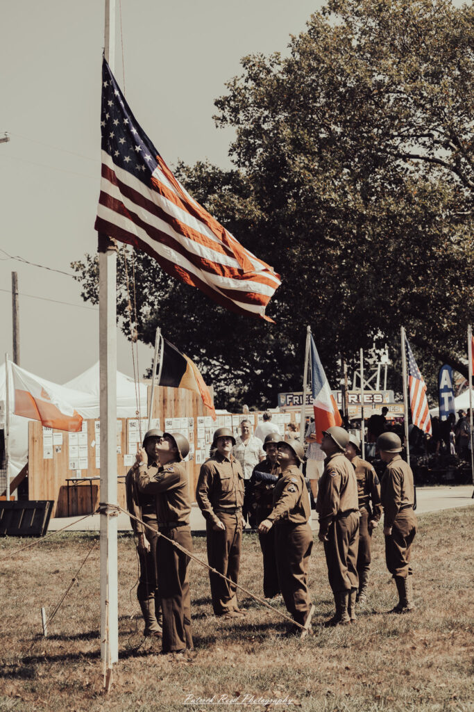 A group of World War II reenactors in period-accurate uniforms—American, German, and French Resistance—on a sandy shore during the D-Day Conneaut 2025 reenactment at Conneaut Township Park, Ohio.