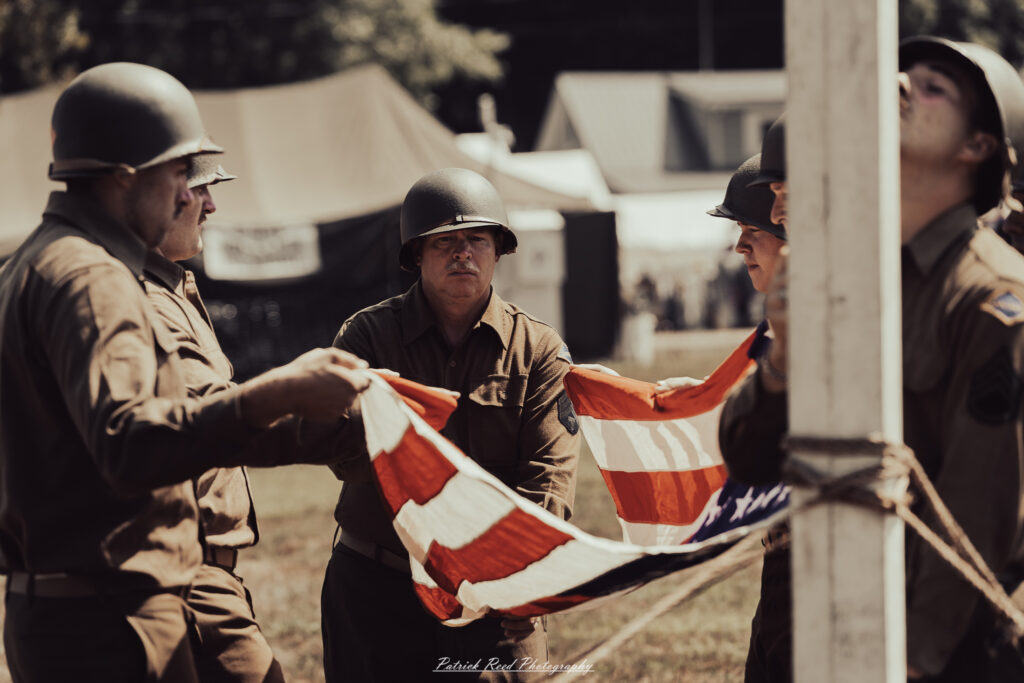 A group of World War II reenactors in period-accurate uniforms—American, German, and French Resistance—on a sandy shore during the D-Day Conneaut 2025 reenactment at Conneaut Township Park, Ohio.