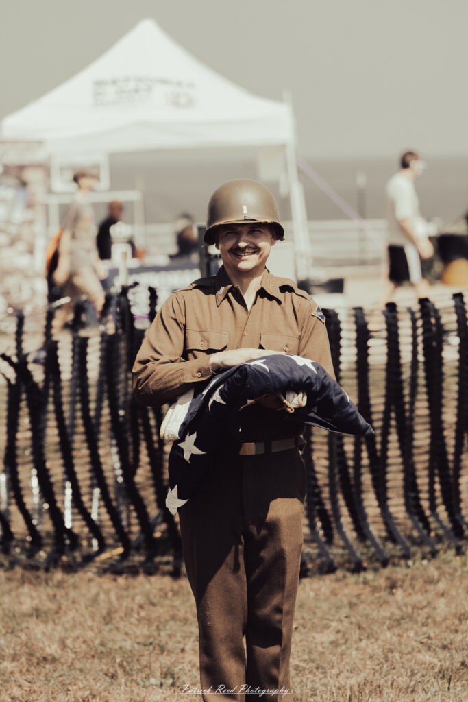 A group of World War II reenactors in period-accurate uniforms—American, German, and French Resistance—on a sandy shore during the D-Day Conneaut 2025 reenactment at Conneaut Township Park, Ohio.
