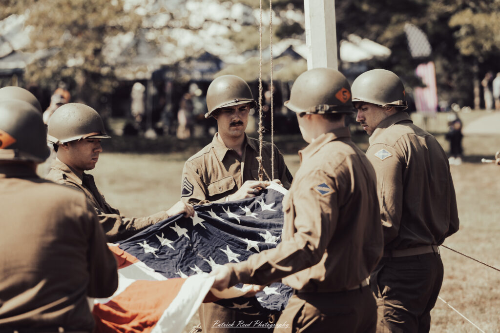 A group of World War II reenactors in period-accurate uniforms—American, German, and French Resistance—on a sandy shore during the D-Day Conneaut 2025 reenactment at Conneaut Township Park, Ohio.