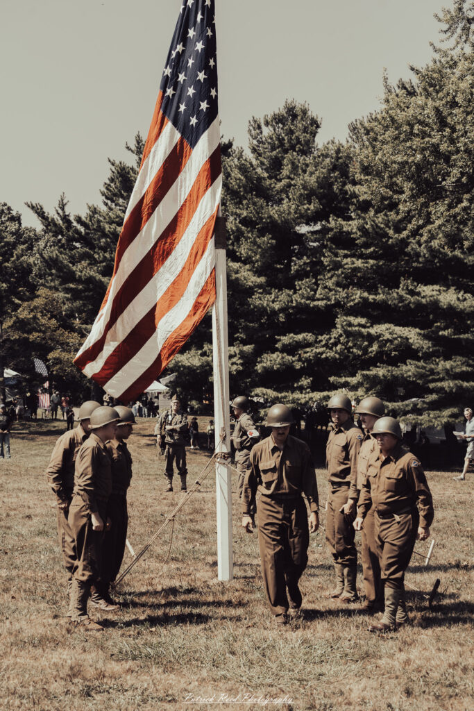 A group of World War II reenactors in period-accurate uniforms—American, German, and French Resistance—on a sandy shore during the D-Day Conneaut 2025 reenactment at Conneaut Township Park, Ohio.