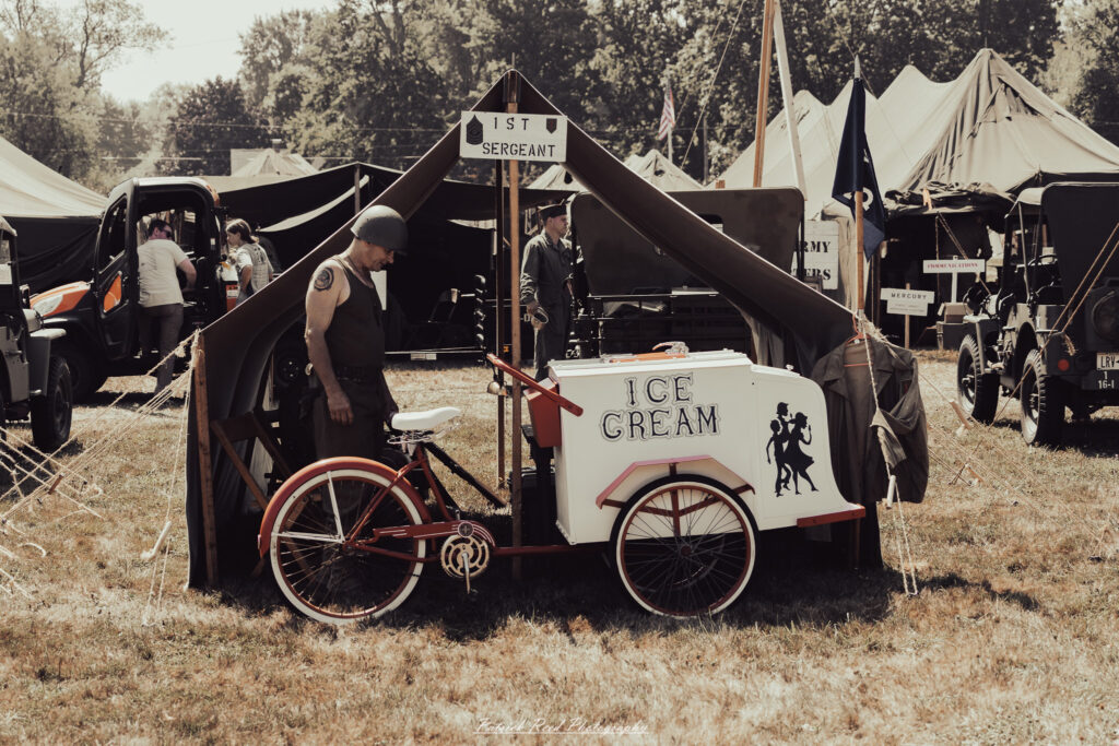 A group of World War II reenactors in period-accurate uniforms—American, German, and French Resistance—on a sandy shore during the D-Day Conneaut 2025 reenactment at Conneaut Township Park, Ohio.