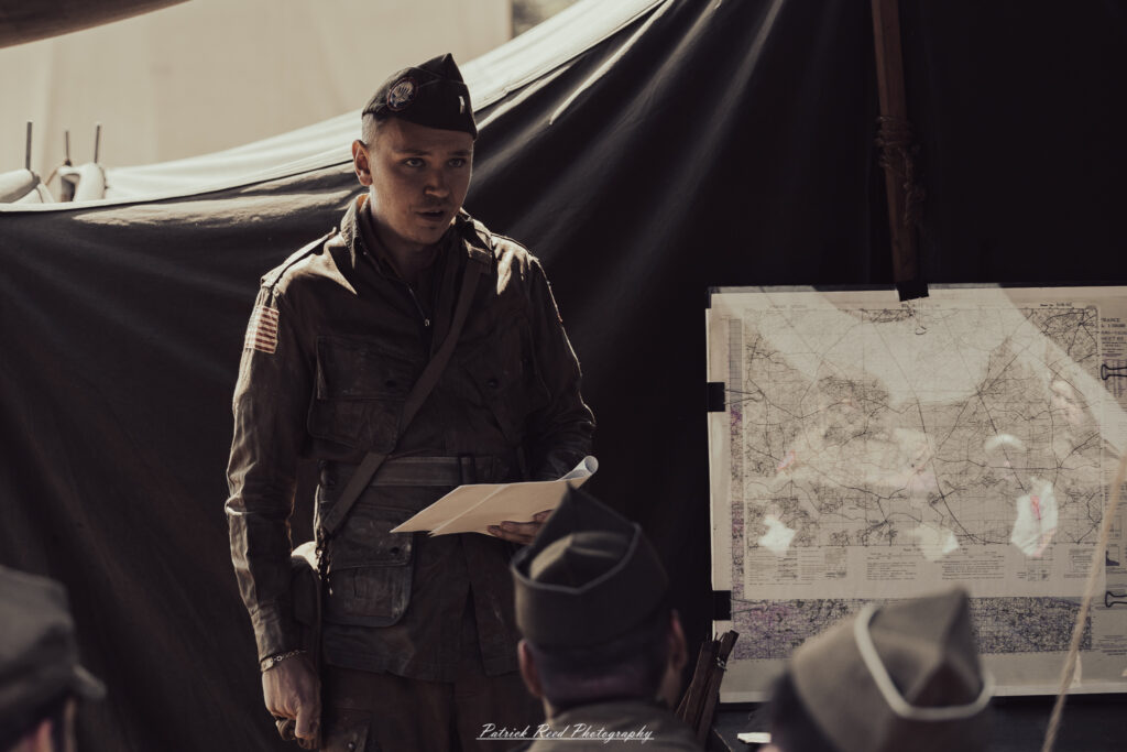 A group of World War II reenactors in period-accurate uniforms—American, German, and French Resistance—on a sandy shore during the D-Day Conneaut 2025 reenactment at Conneaut Township Park, Ohio.