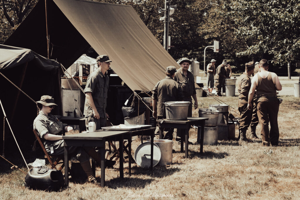 A group of World War II reenactors in period-accurate uniforms—American, German, and French Resistance—on a sandy shore during the D-Day Conneaut 2025 reenactment at Conneaut Township Park, Ohio.
