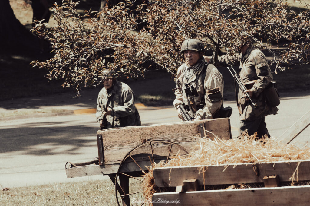 A group of World War II reenactors in period-accurate uniforms—American, German, and French Resistance—on a sandy shore during the D-Day Conneaut 2025 reenactment at Conneaut Township Park, Ohio.