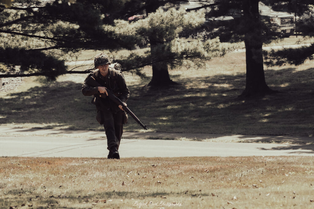 A group of World War II reenactors in period-accurate uniforms—American, German, and French Resistance—on a sandy shore during the D-Day Conneaut 2025 reenactment at Conneaut Township Park, Ohio.