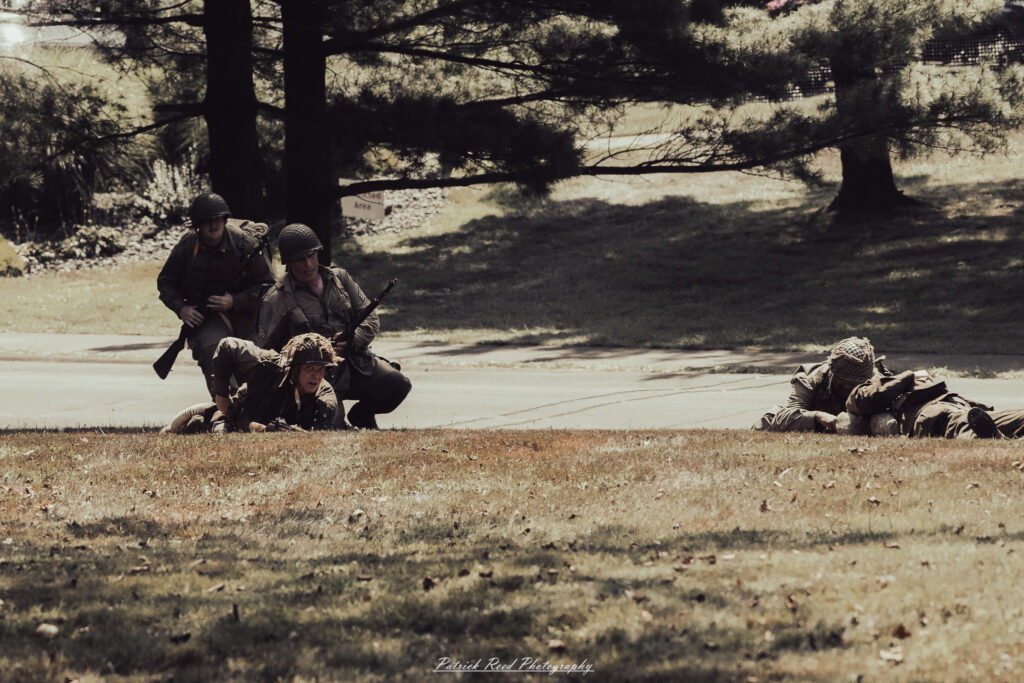 A group of World War II reenactors in period-accurate uniforms—American, German, and French Resistance—on a sandy shore during the D-Day Conneaut 2025 reenactment at Conneaut Township Park, Ohio.