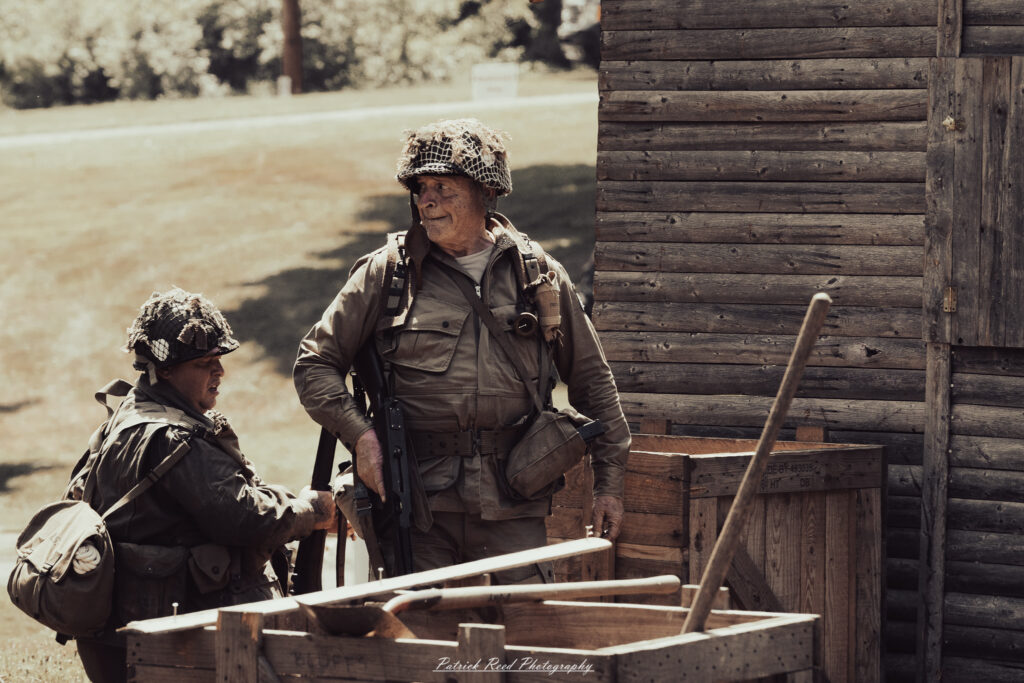A group of World War II reenactors in period-accurate uniforms—American, German, and French Resistance—on a sandy shore during the D-Day Conneaut 2025 reenactment at Conneaut Township Park, Ohio.