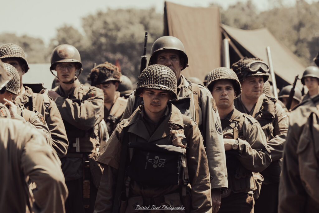 A group of World War II reenactors in period-accurate uniforms—American, German, and French Resistance—on a sandy shore during the D-Day Conneaut 2025 reenactment at Conneaut Township Park, Ohio.