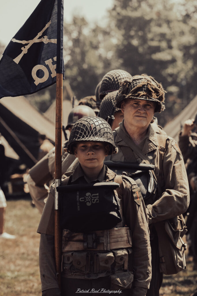 A group of World War II reenactors in period-accurate uniforms—American, German, and French Resistance—on a sandy shore during the D-Day Conneaut 2025 reenactment at Conneaut Township Park, Ohio.