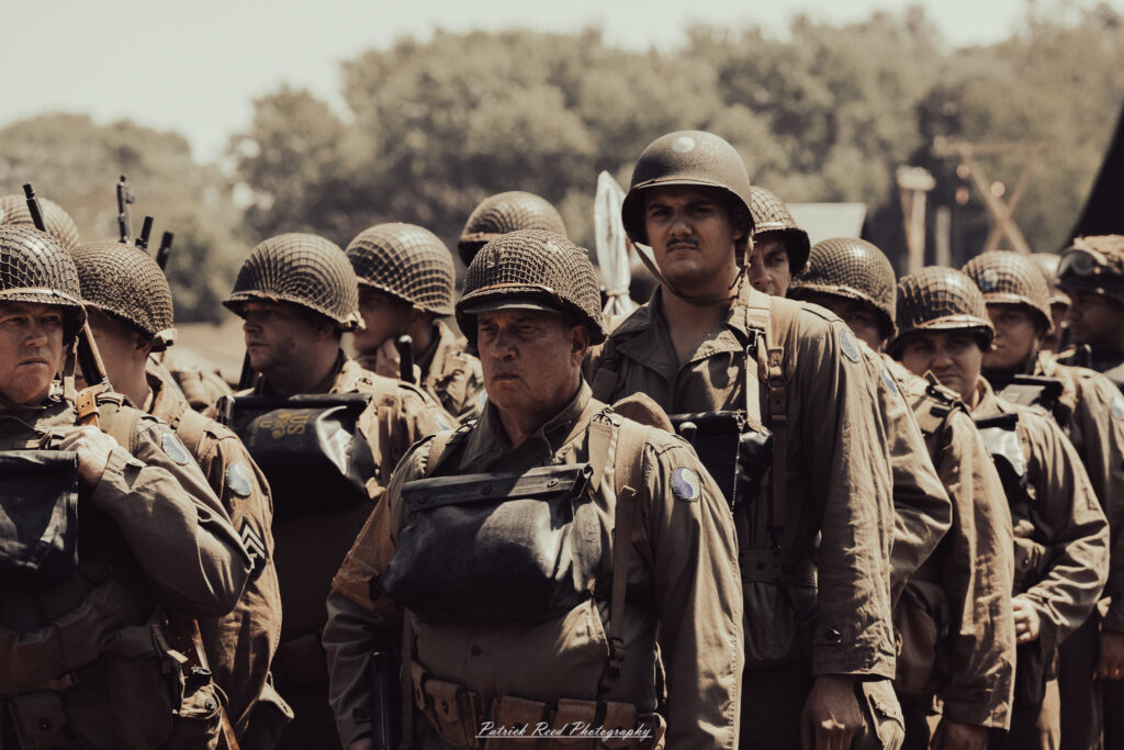 A group of World War II reenactors in period-accurate uniforms—American, German, and French Resistance—on a sandy shore during the D-Day Conneaut 2025 reenactment at Conneaut Township Park, Ohio.