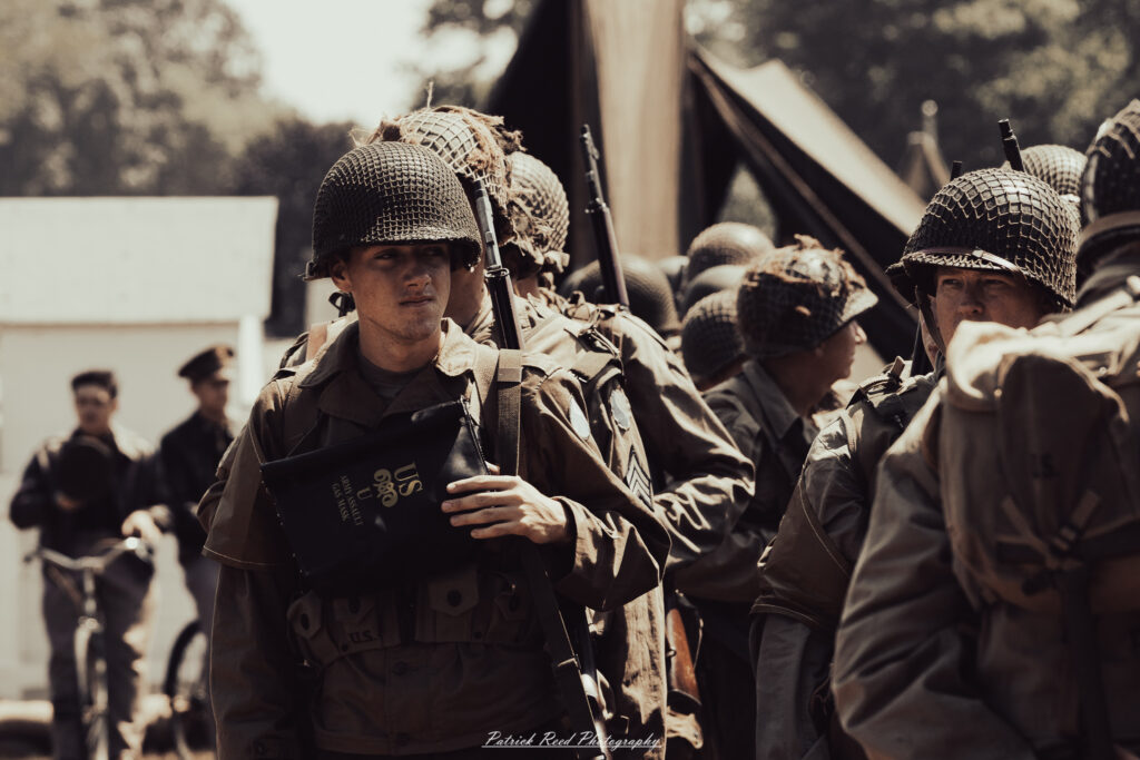 A group of World War II reenactors in period-accurate uniforms—American, German, and French Resistance—on a sandy shore during the D-Day Conneaut 2025 reenactment at Conneaut Township Park, Ohio.