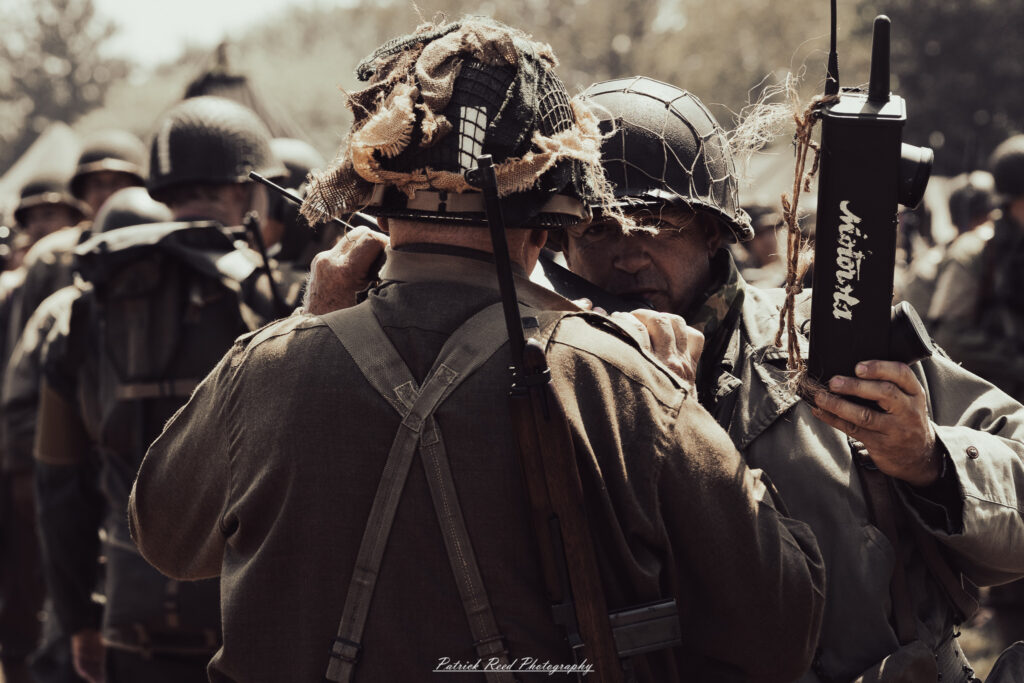 A group of World War II reenactors in period-accurate uniforms—American, German, and French Resistance—on a sandy shore during the D-Day Conneaut 2025 reenactment at Conneaut Township Park, Ohio.