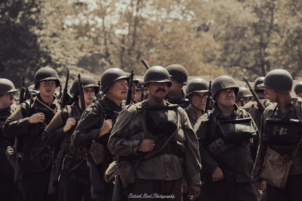A group of World War II reenactors in period-accurate uniforms—American, German, and French Resistance—on a sandy shore during the D-Day Conneaut 2025 reenactment at Conneaut Township Park, Ohio.