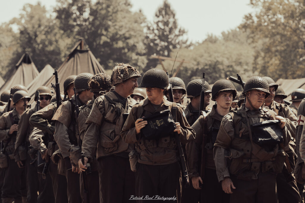 A group of World War II reenactors in period-accurate uniforms—American, German, and French Resistance—on a sandy shore during the D-Day Conneaut 2025 reenactment at Conneaut Township Park, Ohio.