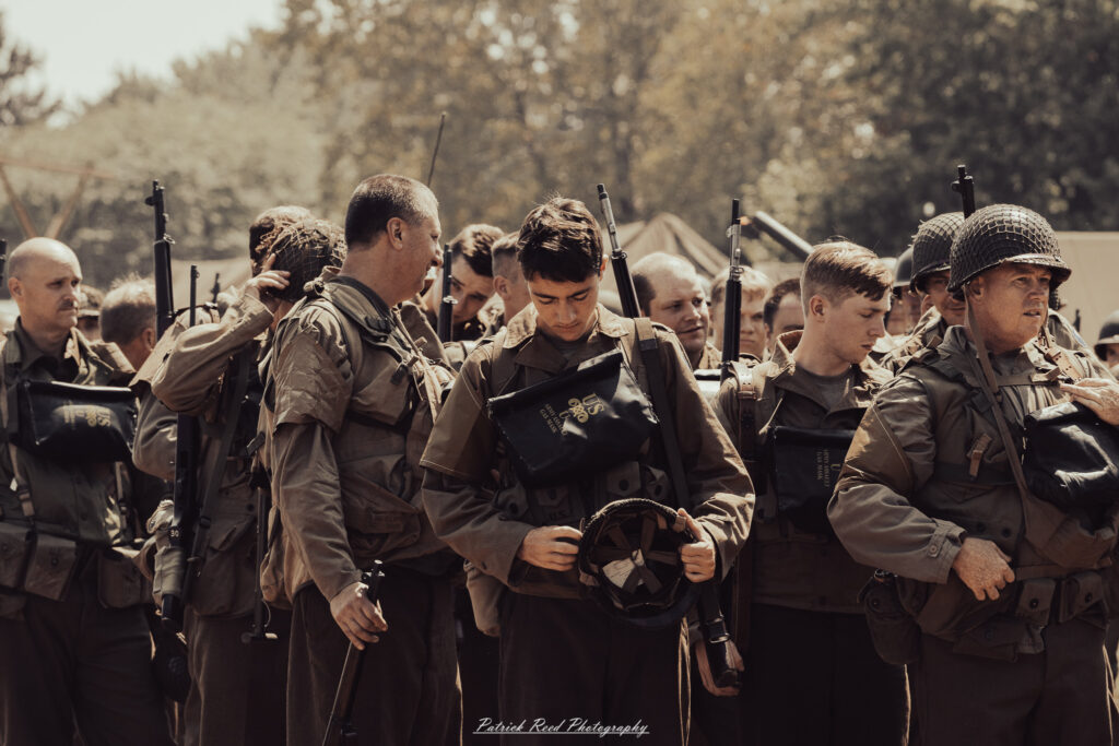 A group of World War II reenactors in period-accurate uniforms—American, German, and French Resistance—on a sandy shore during the D-Day Conneaut 2025 reenactment at Conneaut Township Park, Ohio.