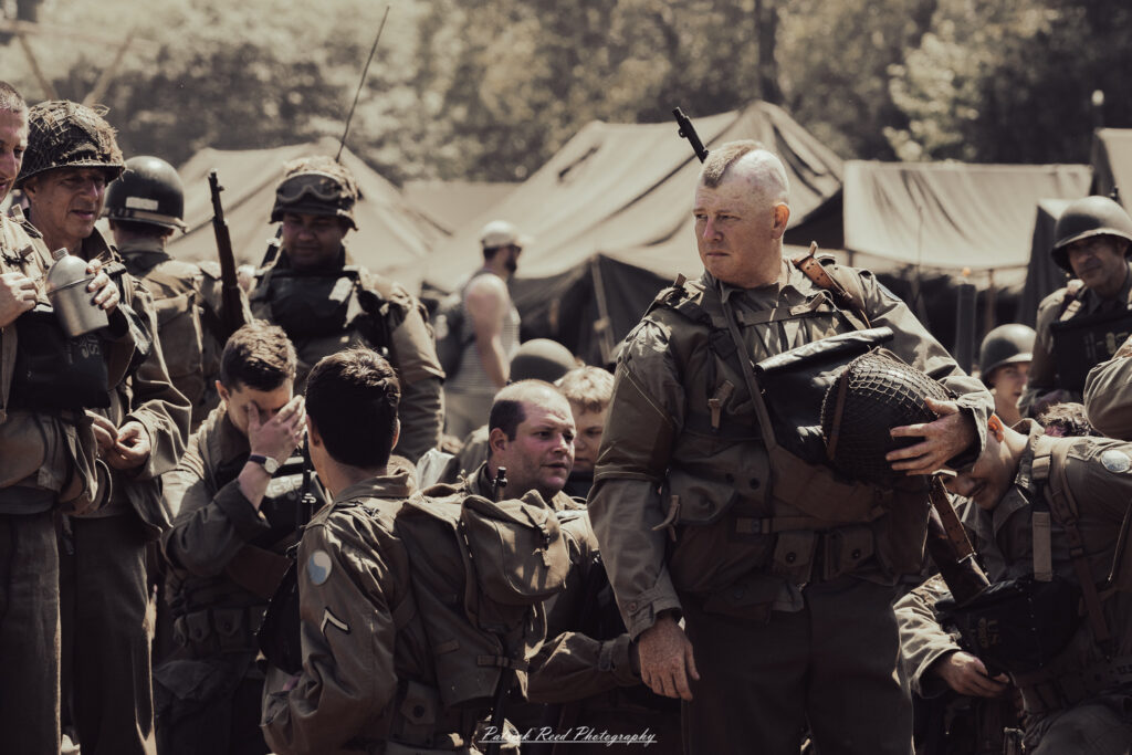 A group of World War II reenactors in period-accurate uniforms—American, German, and French Resistance—on a sandy shore during the D-Day Conneaut 2025 reenactment at Conneaut Township Park, Ohio.