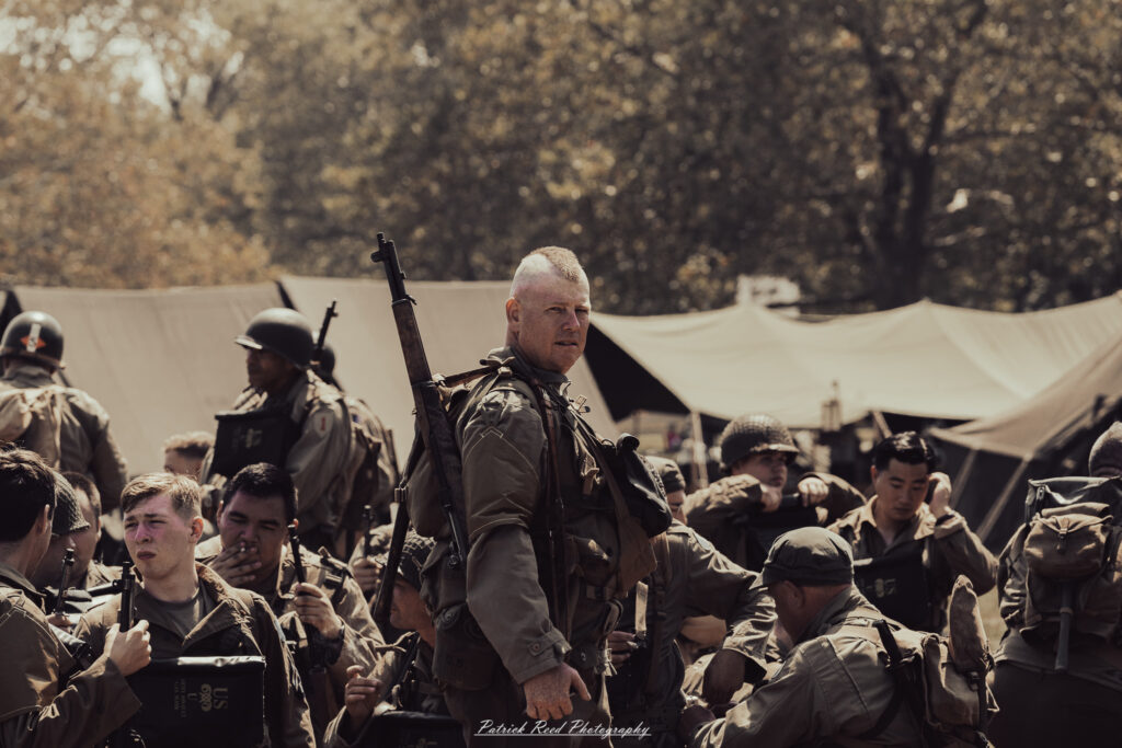 A group of World War II reenactors in period-accurate uniforms—American, German, and French Resistance—on a sandy shore during the D-Day Conneaut 2025 reenactment at Conneaut Township Park, Ohio.