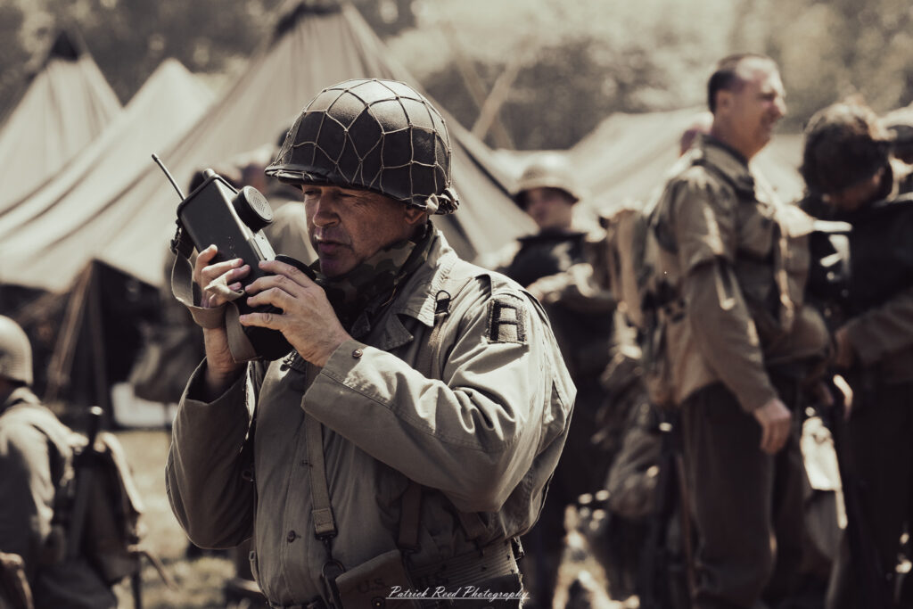 A group of World War II reenactors in period-accurate uniforms—American, German, and French Resistance—on a sandy shore during the D-Day Conneaut 2025 reenactment at Conneaut Township Park, Ohio.