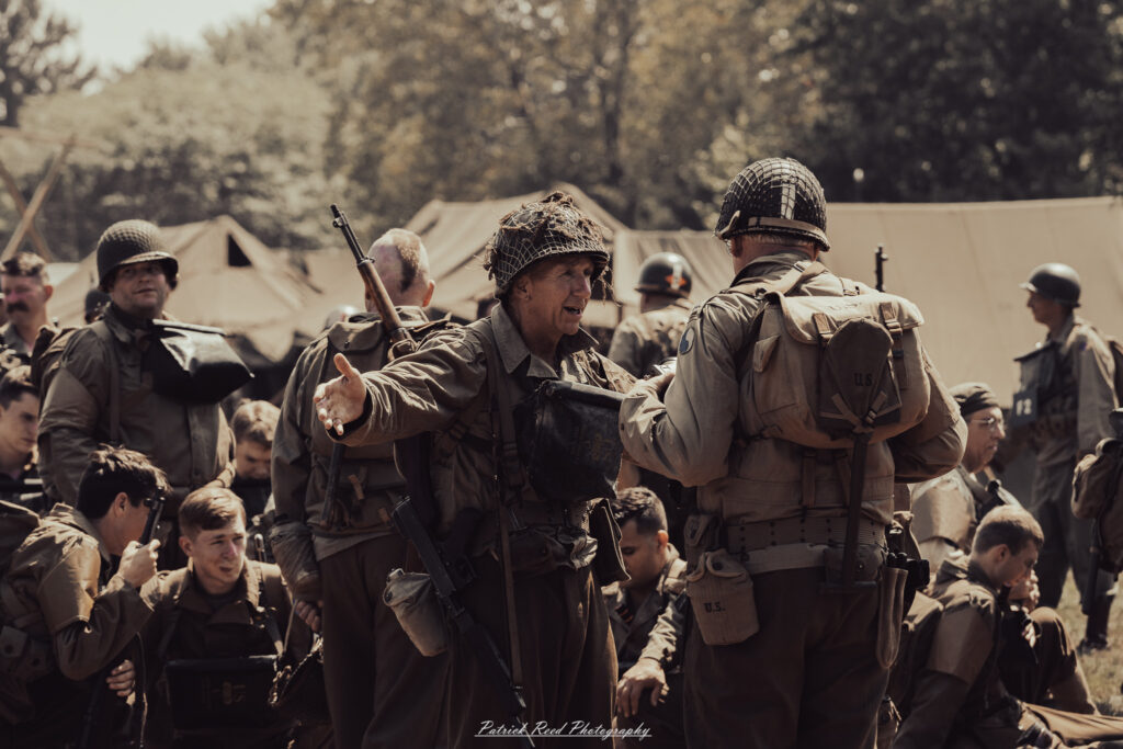 A group of World War II reenactors in period-accurate uniforms—American, German, and French Resistance—on a sandy shore during the D-Day Conneaut 2025 reenactment at Conneaut Township Park, Ohio.