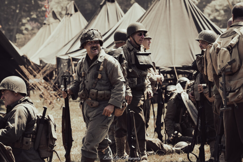 A group of World War II reenactors in period-accurate uniforms—American, German, and French Resistance—on a sandy shore during the D-Day Conneaut 2025 reenactment at Conneaut Township Park, Ohio.