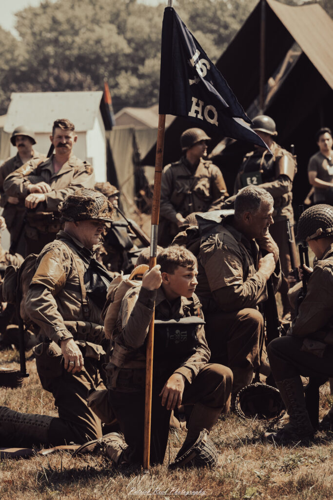 A group of World War II reenactors in period-accurate uniforms—American, German, and French Resistance—on a sandy shore during the D-Day Conneaut 2025 reenactment at Conneaut Township Park, Ohio.