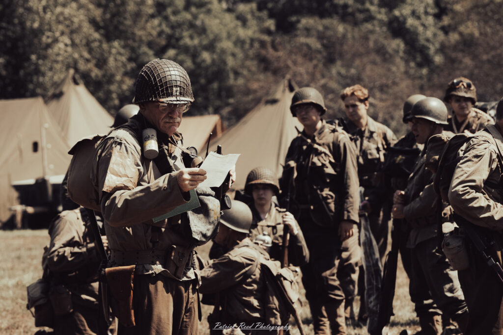 A group of World War II reenactors in period-accurate uniforms—American, German, and French Resistance—on a sandy shore during the D-Day Conneaut 2025 reenactment at Conneaut Township Park, Ohio.