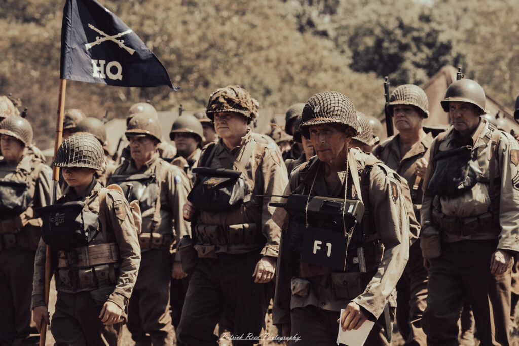 A group of World War II reenactors in period-accurate uniforms—American, German, and French Resistance—on a sandy shore during the D-Day Conneaut 2025 reenactment at Conneaut Township Park, Ohio.
