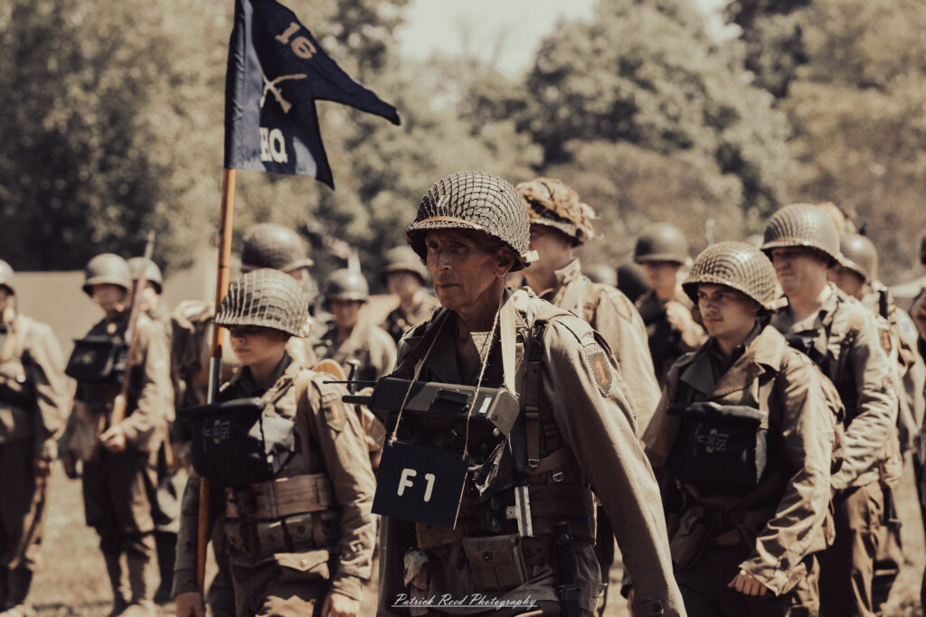 A group of World War II reenactors in period-accurate uniforms—American, German, and French Resistance—on a sandy shore during the D-Day Conneaut 2025 reenactment at Conneaut Township Park, Ohio.