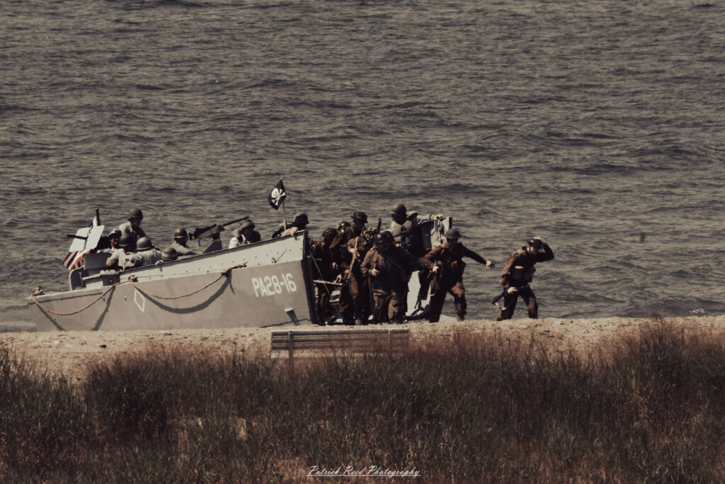 A group of World War II reenactors in period-accurate uniforms—American, German, and French Resistance—on a sandy shore during the D-Day Conneaut 2025 reenactment at Conneaut Township Park, Ohio.