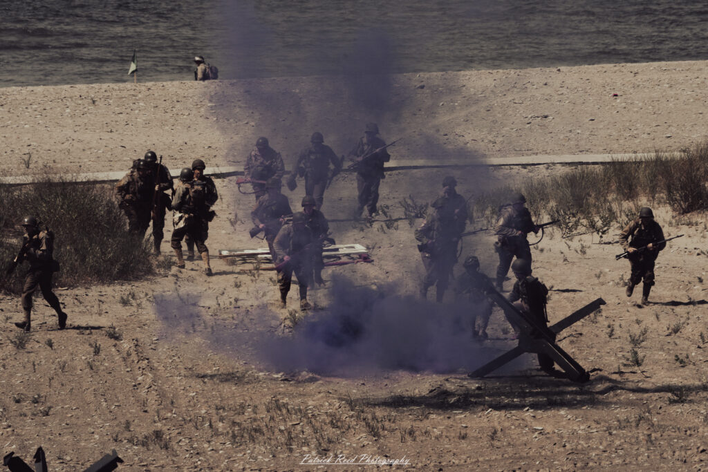 A group of World War II reenactors in period-accurate uniforms—American, German, and French Resistance—on a sandy shore during the D-Day Conneaut 2025 reenactment at Conneaut Township Park, Ohio.