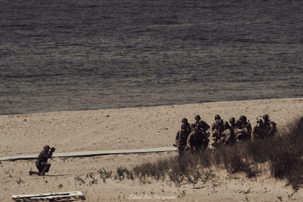 A group of World War II reenactors in period-accurate uniforms—American, German, and French Resistance—on a sandy shore during the D-Day Conneaut 2025 reenactment at Conneaut Township Park, Ohio.