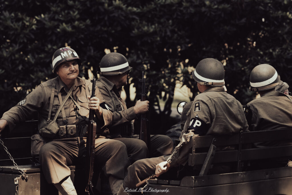 A group of World War II reenactors in period-accurate uniforms—American, German, and French Resistance—on a sandy shore during the D-Day Conneaut 2025 reenactment at Conneaut Township Park, Ohio.