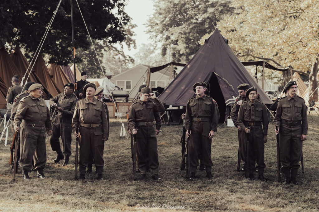 A group of World War II reenactors in period-accurate uniforms—American, German, and French Resistance—on a sandy shore during the D-Day Conneaut 2025 reenactment at Conneaut Township Park, Ohio.