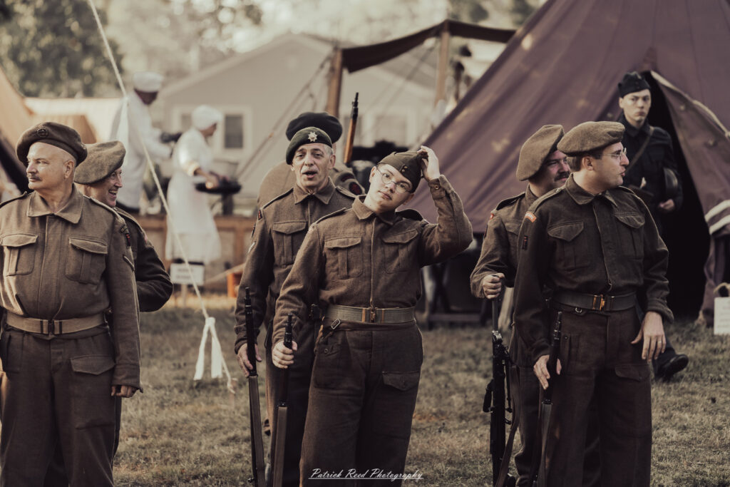 A group of World War II reenactors in period-accurate uniforms—American, German, and French Resistance—on a sandy shore during the D-Day Conneaut 2025 reenactment at Conneaut Township Park, Ohio.