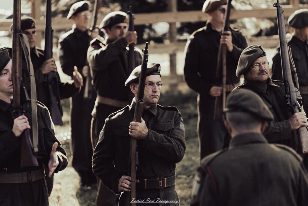 A group of World War II reenactors in period-accurate uniforms—American, German, and French Resistance—on a sandy shore during the D-Day Conneaut 2025 reenactment at Conneaut Township Park, Ohio.