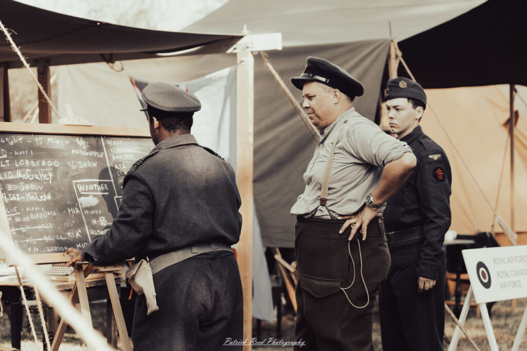A group of World War II reenactors in period-accurate uniforms—American, German, and French Resistance—on a sandy shore during the D-Day Conneaut 2025 reenactment at Conneaut Township Park, Ohio.