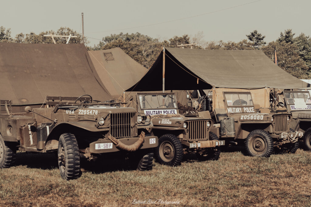 A group of World War II reenactors in period-accurate uniforms—American, German, and French Resistance—on a sandy shore during the D-Day Conneaut 2025 reenactment at Conneaut Township Park, Ohio.