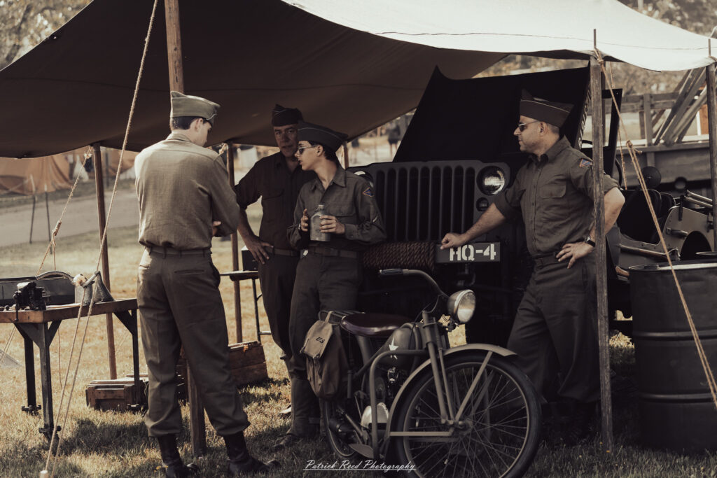 A group of World War II reenactors in period-accurate uniforms—American, German, and French Resistance—on a sandy shore during the D-Day Conneaut 2025 reenactment at Conneaut Township Park, Ohio.