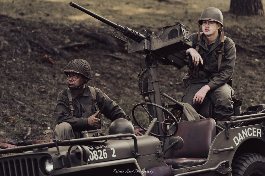 A group of World War II reenactors in period-accurate uniforms—American, German, and French Resistance—on a sandy shore during the D-Day Conneaut 2025 reenactment at Conneaut Township Park, Ohio.
