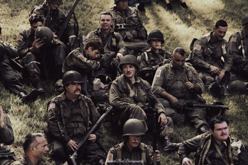 A group of World War II reenactors in period-accurate uniforms—American, German, and French Resistance—on a sandy shore during the D-Day Conneaut 2025 reenactment at Conneaut Township Park, Ohio.