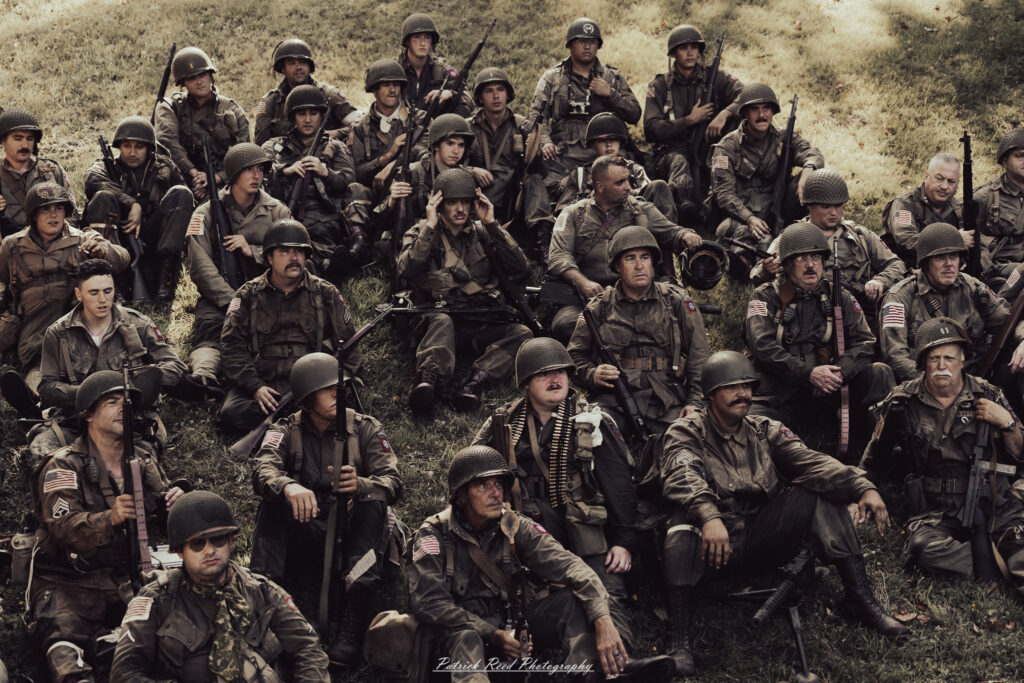A group of World War II reenactors in period-accurate uniforms—American, German, and French Resistance—on a sandy shore during the D-Day Conneaut 2025 reenactment at Conneaut Township Park, Ohio.