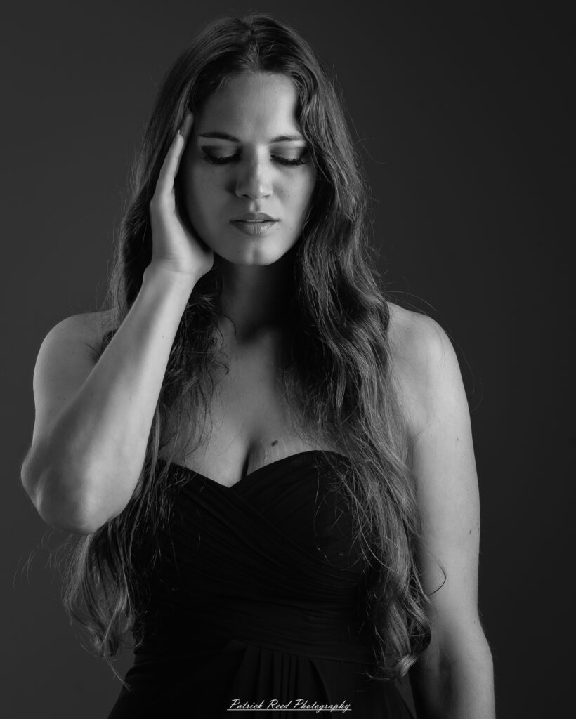 A studio portrait a poised female model in a sleek black dress, photographed under controlled lighting on August 23, 2025.
