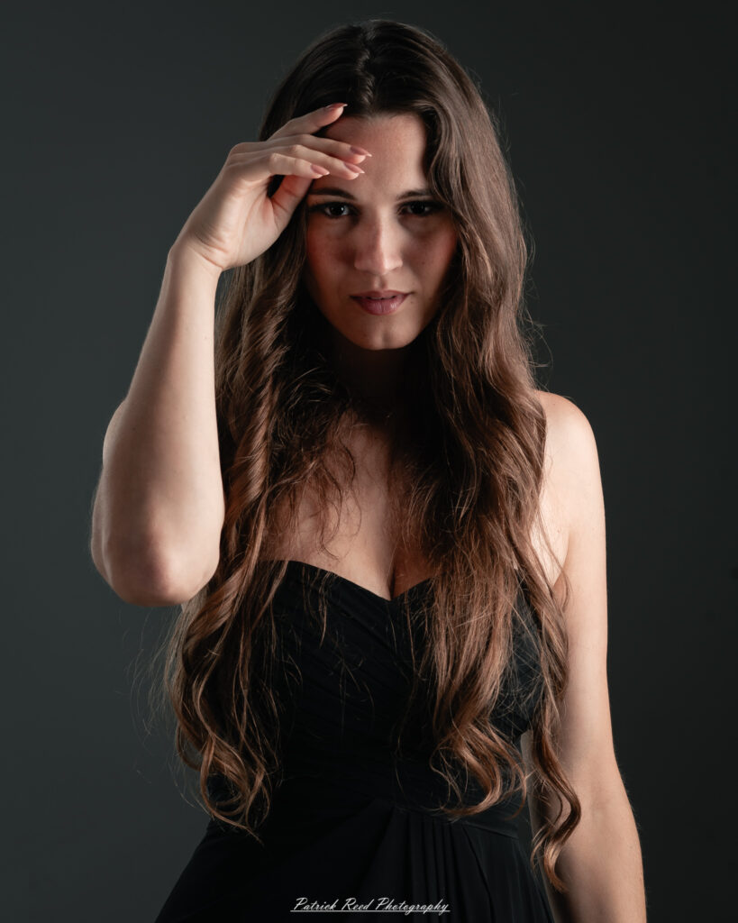 A studio portrait a poised female model in a sleek black dress, photographed under controlled lighting on August 23, 2025.